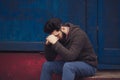 Stressed and upset young man sitting outside holding head with a hand looking down. Human emotion feelings, sad bearded Royalty Free Stock Photo