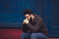 Stressed and upset young man sitting outside holding head with a hand looking down. Human emotion feelings, sad bearded Royalty Free Stock Photo