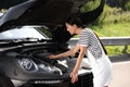 Stressed woman looking under hood of broken car outdoors Royalty Free Stock Photo