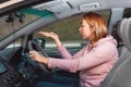 A stressed woman is sitting behind the wheel of a car and cursing, points to the road with her hand. Side view. Royalty Free Stock Photo