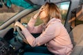 A stressed woman is sitting behind the wheel of a car and holding her head in despair. Royalty Free Stock Photo