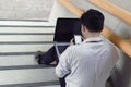 Stressed young Asian business man sitting and using mobile smart phone and laptop at staircase of office Royalty Free Stock Photo