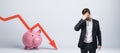 Stressed businessman with falling red chart arrow with piggy bank on white background. Economic recession, losing savings Royalty Free Stock Photo