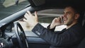 Stressed businessman swearing and talking phone while sitting inside car outdoors