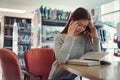 Stressed young female student sitting at wooden table and reading book during exam preparation in library Royalty Free Stock Photo