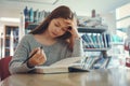 Stressed young female student sitting at wooden table and reading book during exam preparation in library Royalty Free Stock Photo