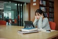 Stressed young female student sitting at wooden table and reading book during exam preparation in library Royalty Free Stock Photo