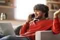 Stressed Young Indian Man Talking On Cellphone And Using Laptop At Home Royalty Free Stock Photo