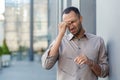 Stressed young man with a headache rubbing temples, feeling pressure, urban background Royalty Free Stock Photo