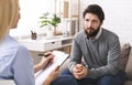 Stressed young man talking to psychologist at therapy