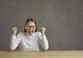 Stressed young woman with eyes closed screaming clenching fist sitting at desk Royalty Free Stock Photo