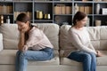 Stressed young woman sitting separately with offended mature mother.