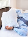 The stresses of business. A businessman covering his face with a pillow.