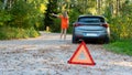 Stressful young woman driver hitchhikes and stops cars, asks for help as have problem with brocken car, uses red triangle sign Royalty Free Stock Photo