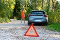 Stressful young woman driver hitchhikes and stops cars, asks for help as have problem with brocken car, uses red triangle sign Royalty Free Stock Photo