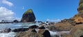 A stretch of black rocks on the beach with a blue sky and white clouds in the background