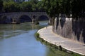 Stretch of river with bridge and embankment, on a sunny day, with an incidental unrecognizable person