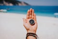 Stretched hand palm with black metal compass against summer beach and blue sea. Follow your way, goal, wish concept