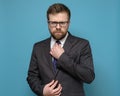 Strict, confident business man straightens his tie and with piercing eyes looks into the camera, on a blue background.