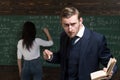 Strict professor looking at students over the glasses while holding book and piece of chalk in his hands. Female student Royalty Free Stock Photo