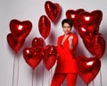 Strict woman in red pantsuit stands surrounded by red heart air balloon showing threaten gesture sign with her fist Royalty Free Stock Photo