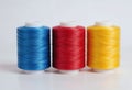 Three spools of thread in vibrant blue, red, and yellow against a neutral background