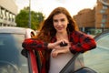 A striking red-haired girl stands next to a red car on the street holding the car keys