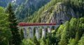 Iconic Red Train Crossing a Stone Arch Bridge Through a Lush Green Mountainous Forest Landscape Royalty Free Stock Photo