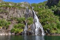 Cascading waterfall in Trollfjorden, Lofoten, bathed in sunlight amidst lush greenery Royalty Free Stock Photo