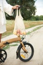 String bag with apples weighs on the handlebars of a folding bicycle. Next a girl in white linen suit. The concept of a