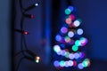 String of Christmas lights hanging on the wall, with defocused xmas tree in the background. Christmas lights bokeh. Royalty Free Stock Photo