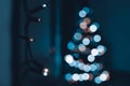 String of Christmas lights hanging on the wall, with defocused xmas tree in the background. Christmas lights bokeh. Royalty Free Stock Photo