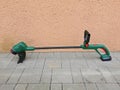 String electric lawnmower, trimmer, green plastic body, placed on concrete pavement by the wall of the house Royalty Free Stock Photo