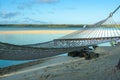 String hammock slung in shade over tropical beach