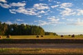 A strip of asphalt gives way to a meadow with freshly cut haystacks, and behind them the edge of the forest and the sky with white