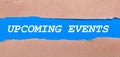 A strip of blue paper with the inscription UPCOMING EVENTS between the brown paper. View from above Royalty Free Stock Photo