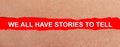 A strip of red paper under the torn brown paper. White lettering on red paper WE ALL HAVE STORIES TO TELL. View from above