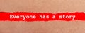 A strip of red paper under the torn brown paper. White lettering on red paper EVERYONE HAS A STORY. View from above Royalty Free Stock Photo