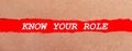 A strip of red paper under the torn brown paper. White lettering on red paper KNOW YOUR ROLE. View from above Royalty Free Stock Photo