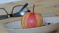 The striped apple lies in a plate on the table with a yellow tablecloth. Food. Background picture.