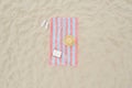 Striped beach towel, book, straw hat and flip flops on sand, aerial view