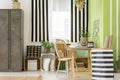 Striped bed next to wooden chair at desk in green workspace interior with cabinet. Real photo Royalty Free Stock Photo