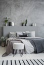 Striped carpet and stool in grey bedroom interior with sheets on