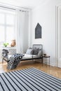 Striped carpet in white bedroom interior with patterned blanket on bed near window