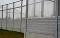 Striped glass noise barrier made of metal perforated sheet metal slats. gray and silver protective fencing separates housing from