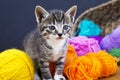 A striped kitten plays with balls of wool. Wicker basket, wooden floor and black background. Royalty Free Stock Photo