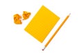 A striped notebook with orange sheets next to which lies a sharpened pencil and two crumpled pieces of paper on white background.