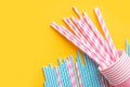 Striped pink and white blue paper drinking straws pink cups on bright yellow background. Kids birthday party celebration Royalty Free Stock Photo