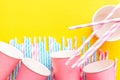 Striped Pink And White Blue Polka Dot Paper Drinking Straws Pink Cups On Bright Yellow Background. Kids Birthday Party Celebration