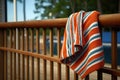 a striped pool towel hanging on a rusty nail against a wooden deck railing